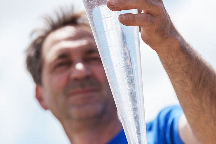 Mitarbeiter von BauGrund Süd hält Wasserprobe in einem Messzylinder vor blauem Himmel