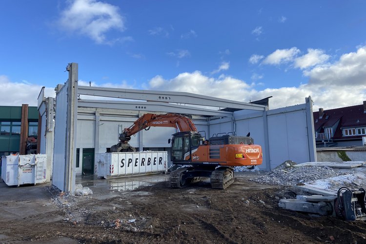 Ein Bagger lädt Bauschutt von einem Gebäuderückbau in einen Container