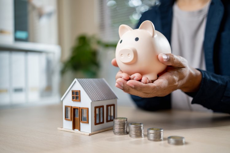 Modellhaus mit Sparschwein und Lupe auf einem Bauplan als Symbol für KfW-Förderung und Baufinanzierung