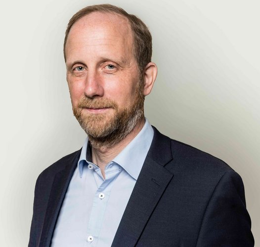 Porträt von Dr. Martin Sabel im dunklen Sakko und hellblauen Hemd vor hellem Hintergrund.