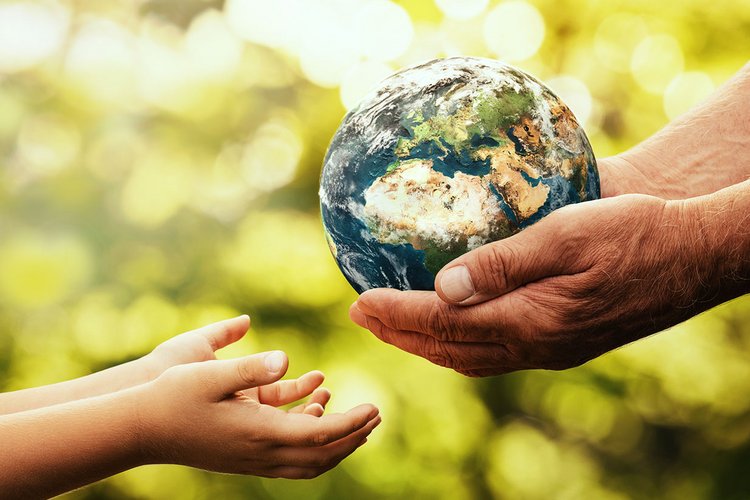 Erwachsene Hände reichen ein Weltkugel an Kinderhände weiter.