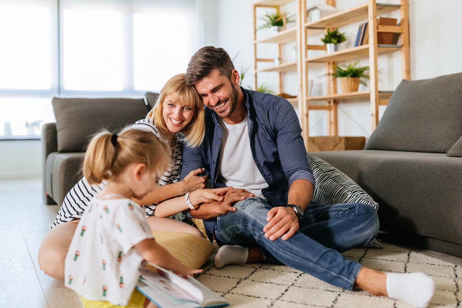 Ein junges Ehepaar sitzt mit einem kleinen Mädchen auf dem Parkettfußboden eines modernen Wohnzimmers