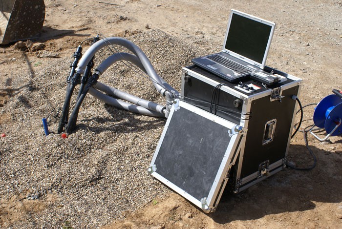Laptop und mobile Messanlage mit angeschlossenen Schläuchen zur Überwachung von Bodenarbeiten und Durchführung eines Thermal Response Test auf einer Baustelle.