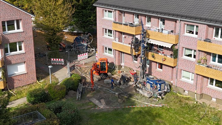 Baustelle für Geothermie-Bohrung vor Mehrfamilienhäusern mit Bohrgerät, Bagger und Arbeitern im Einsatz