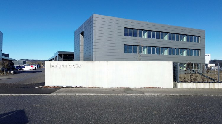 Modernes Bürogebäude von Baugrund Süd mit grauer Fassade, großen Fensterfronten und Firmenschild vor dem Eingang
